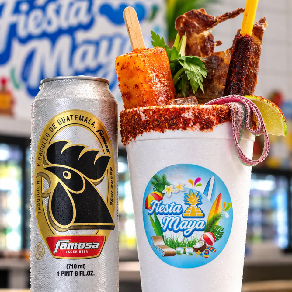 Famosa beer can beside a chili-rimmed Fiesta Maya cocktail garnished with skewered snacks, herbs, lime, and candy.